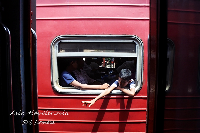 スリランカの赤い列車の窓から身を乗り出す男の子