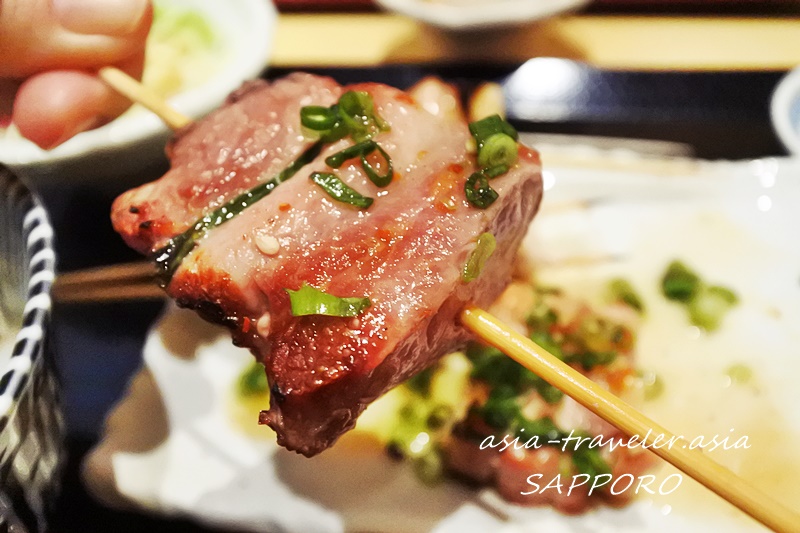 串に刺さった豚精の焼き鳥をつまみ上げる箸アップ