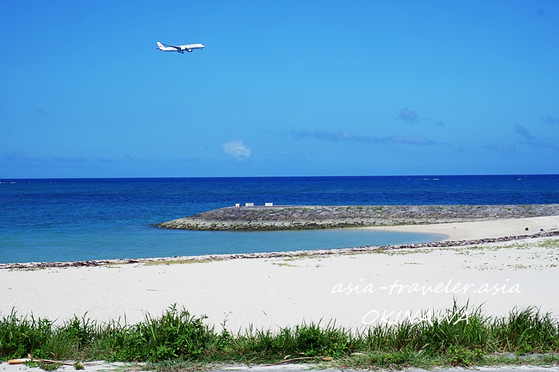 美らサンビーチ上空を飛行機が着陸態勢で通過する青空と白砂浜