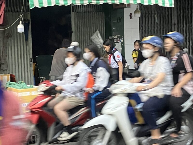 ホーチミンの早朝、マスク姿の学生たちがバイクで通学する様子