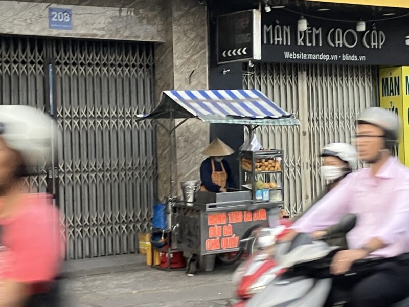 ホーチミン路上のバインミー屋台と通り過ぎるバイク