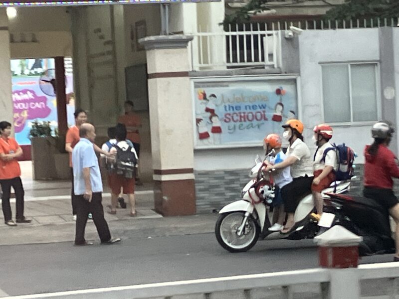 ホーチミン市内をバイクで通学する親子と学校前の朝の風景
