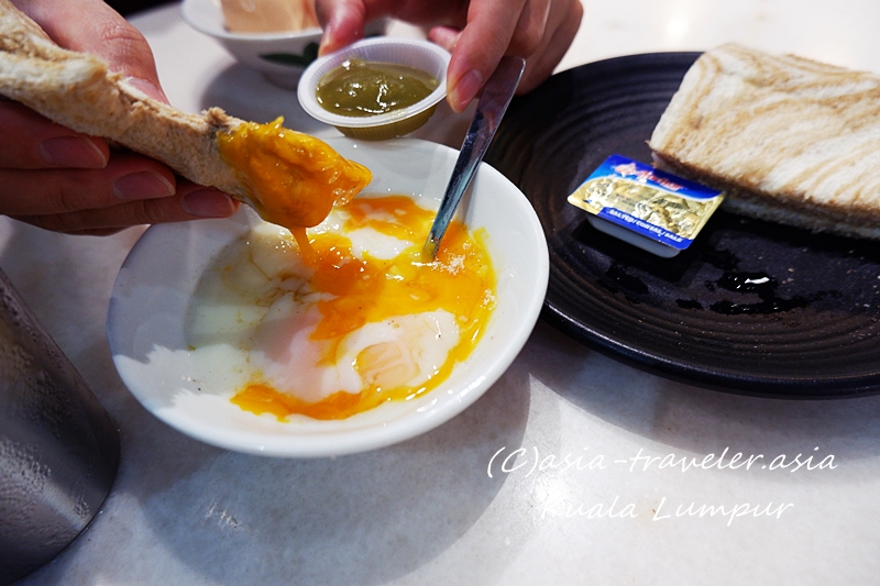 クアラルンプールのコピティアムでカヤトーストを半熟卵にディップする様子
