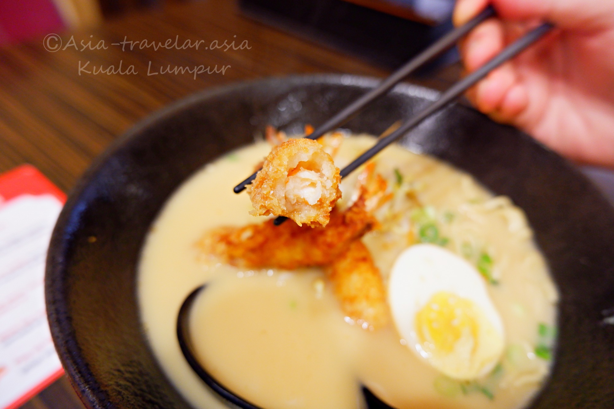 クアラルンプール「1番ラーメン」の海老フライラーメンを箸でつまむ様子