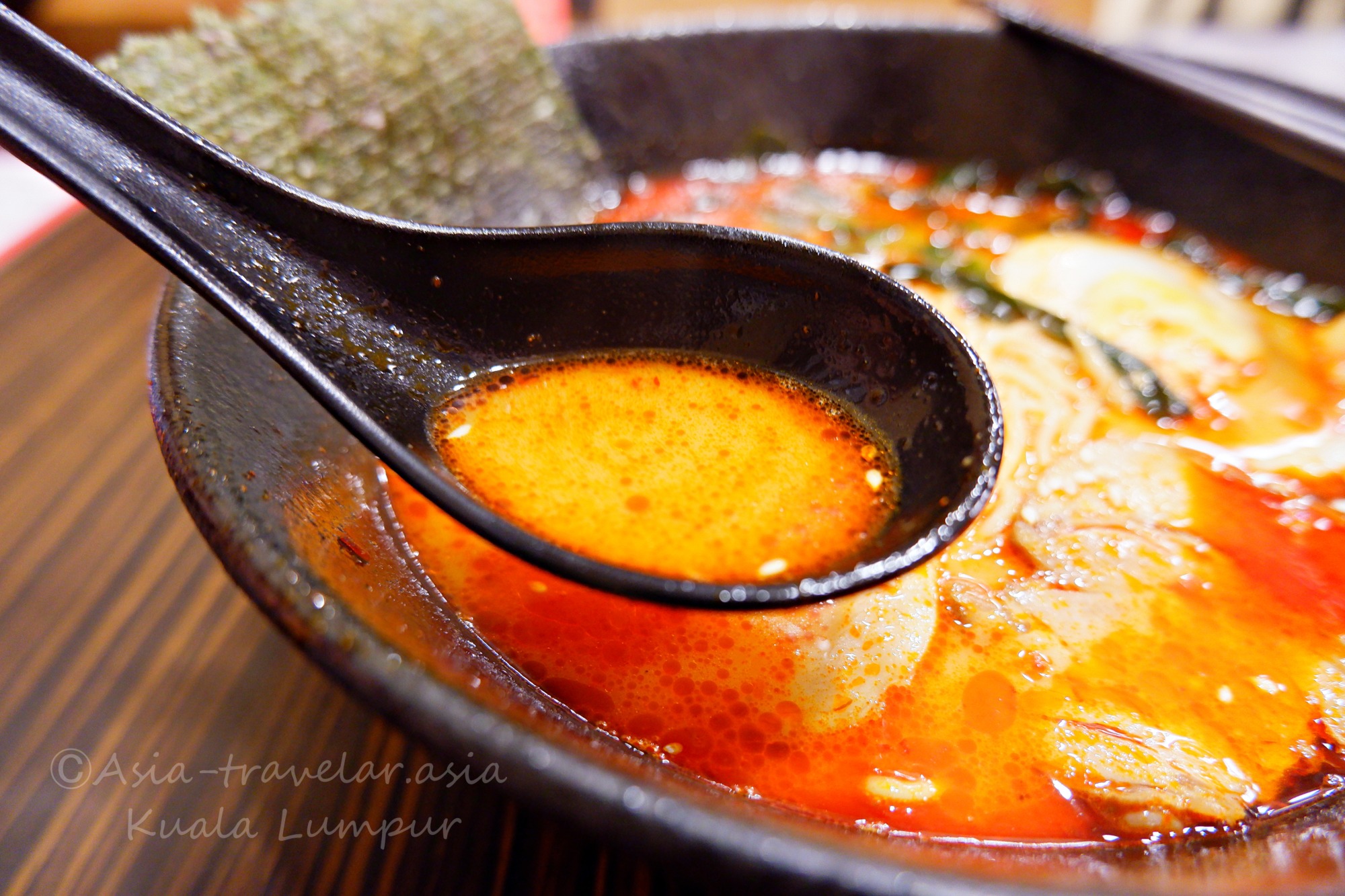 クアラルンプール・1番ラーメンの真っ赤な辛味スープをレンゲで掬うアップ
