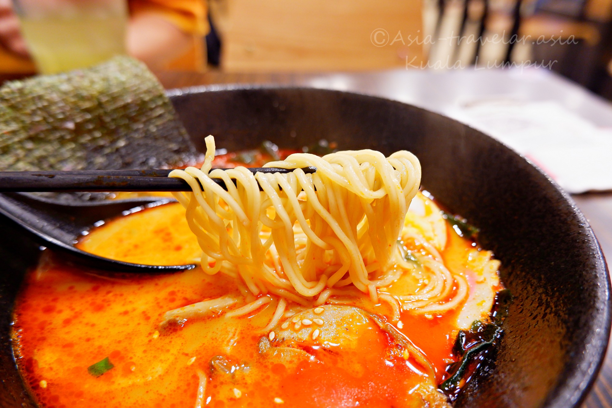 クアラルンプール・1番ラーメンの赤辛スープと箸で持ち上げた麺