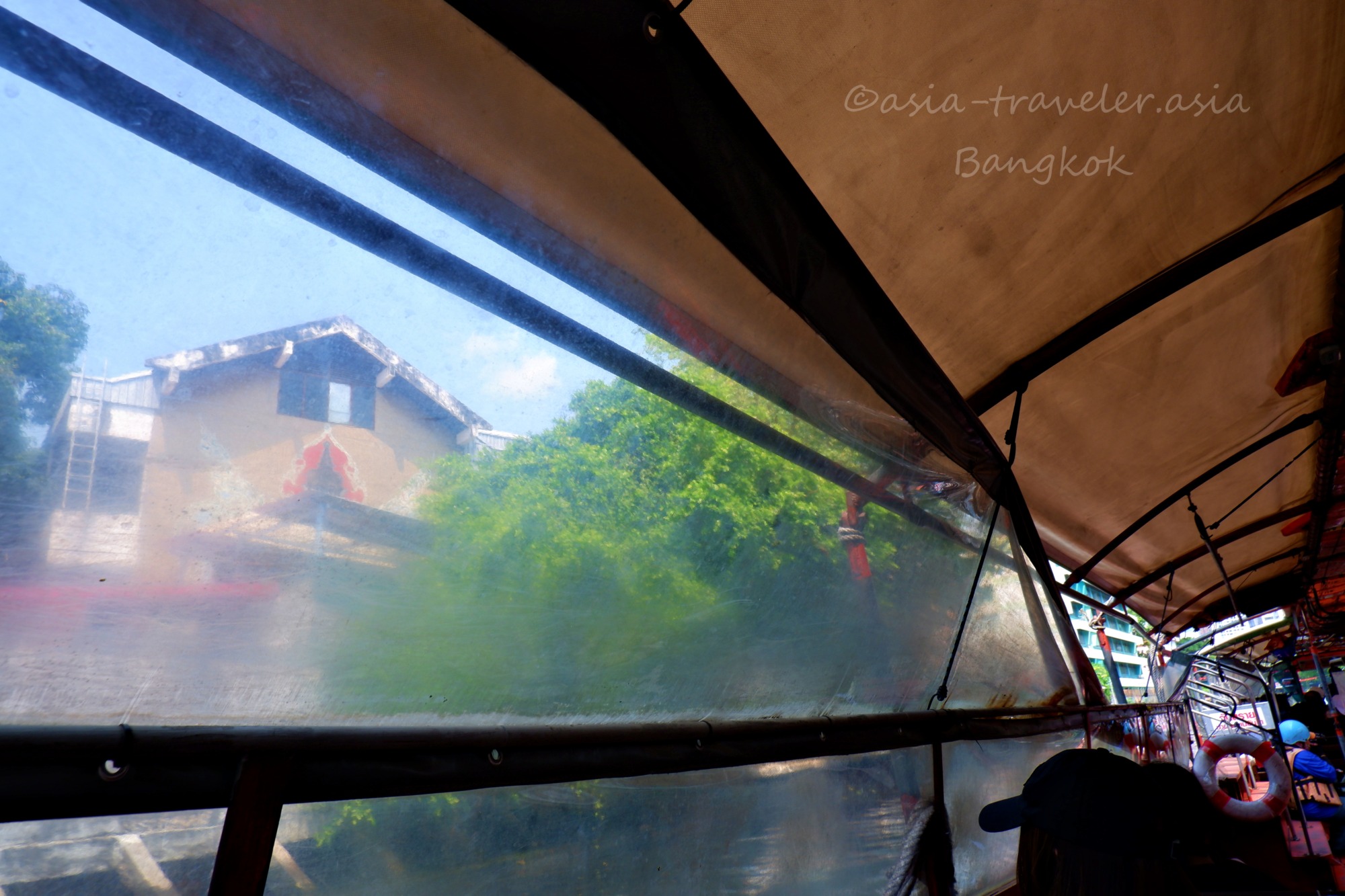 バンコク・センセープ運河水上バス車内からビニールシート越しに見る沿岸の寺院と緑