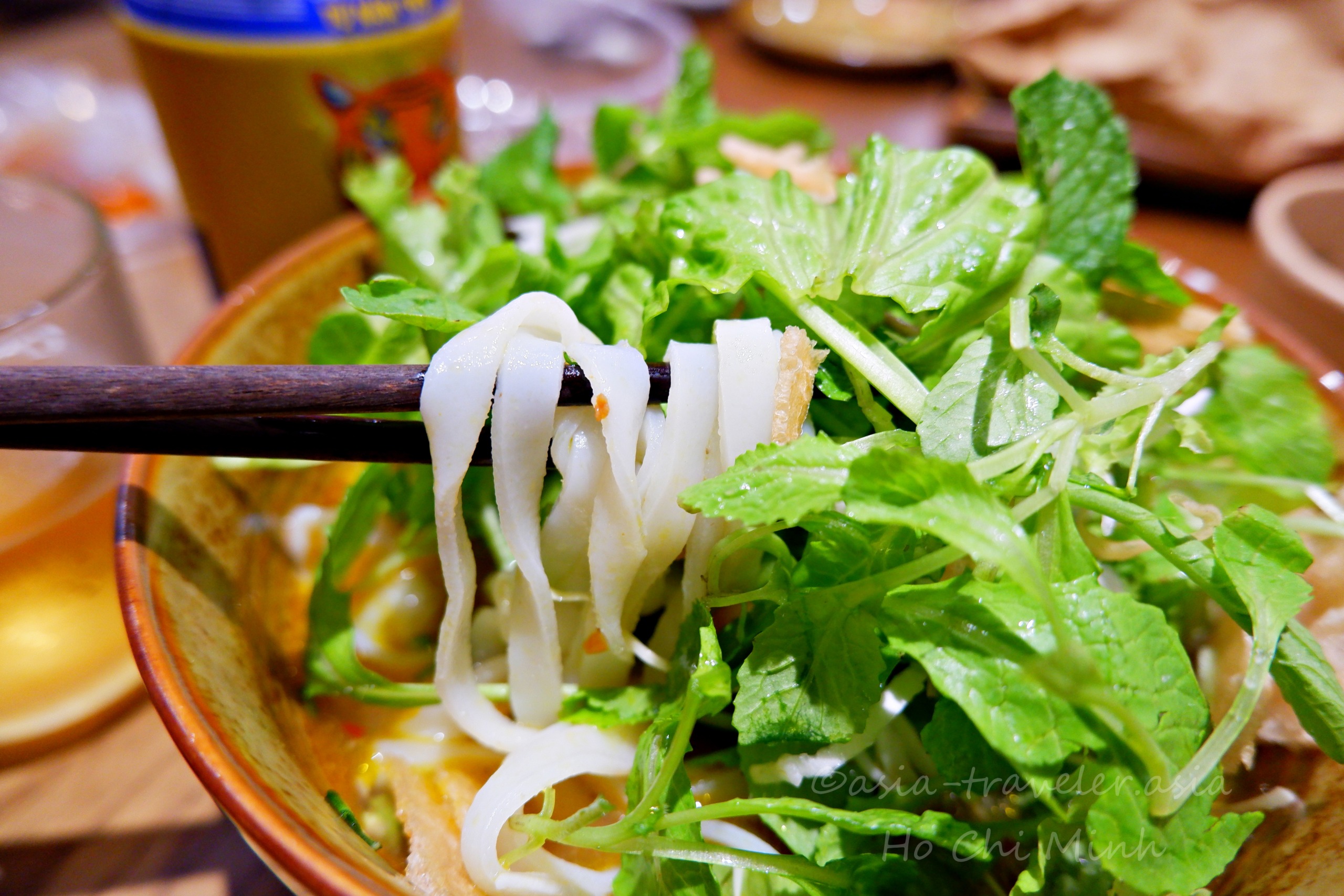 箸で持ち上げたミークアンの平打ち米麺と新鮮なハーブ