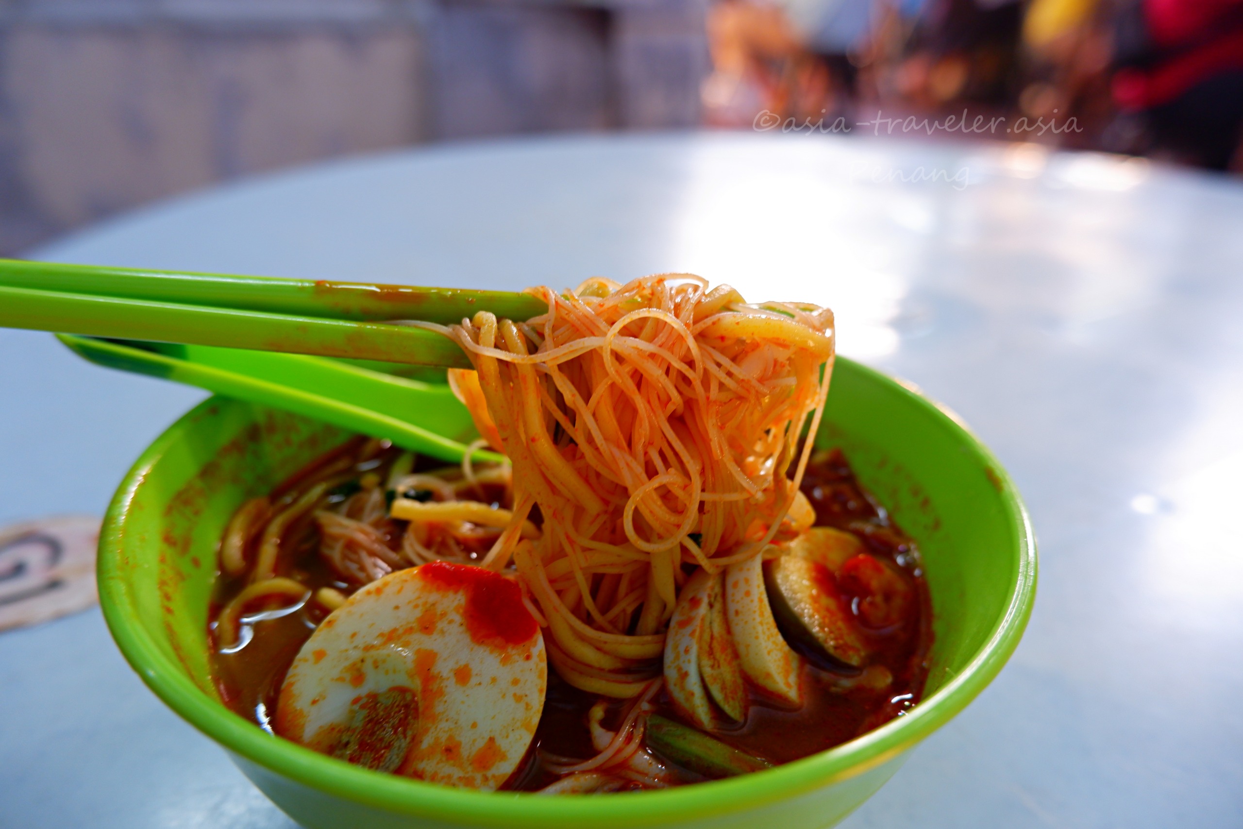 ペナン島ジェルトン朝市の福建麵を箸で持ち上げた赤いスープ麺