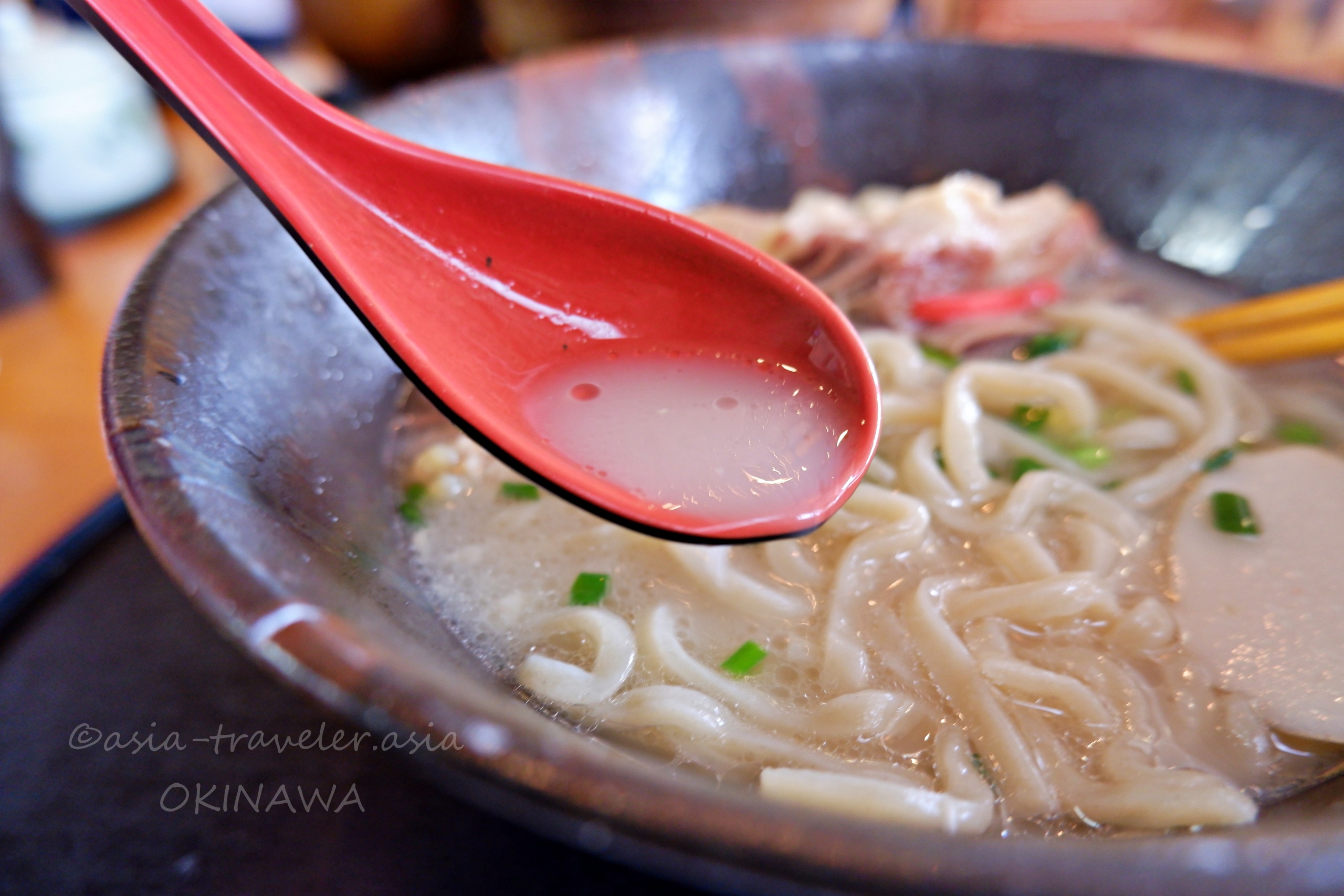 月桃の豚骨白濁スープと沖縄そばを赤レンゲで掬う