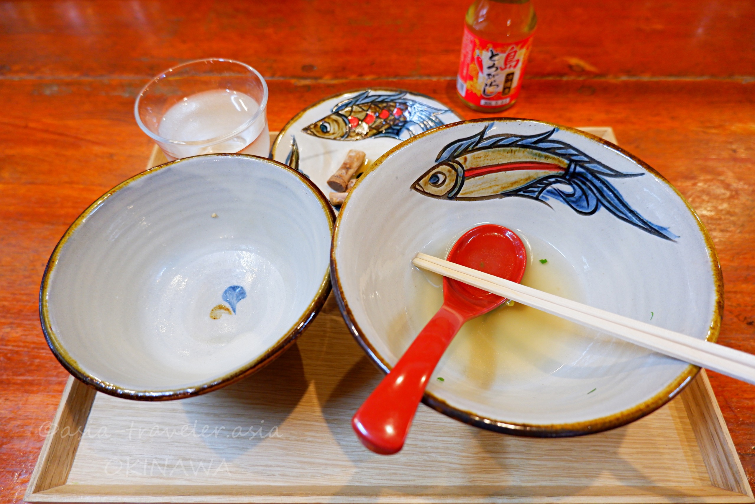 食べ終えた沖縄そばの器と赤いレンゲが木製トレーに並ぶ