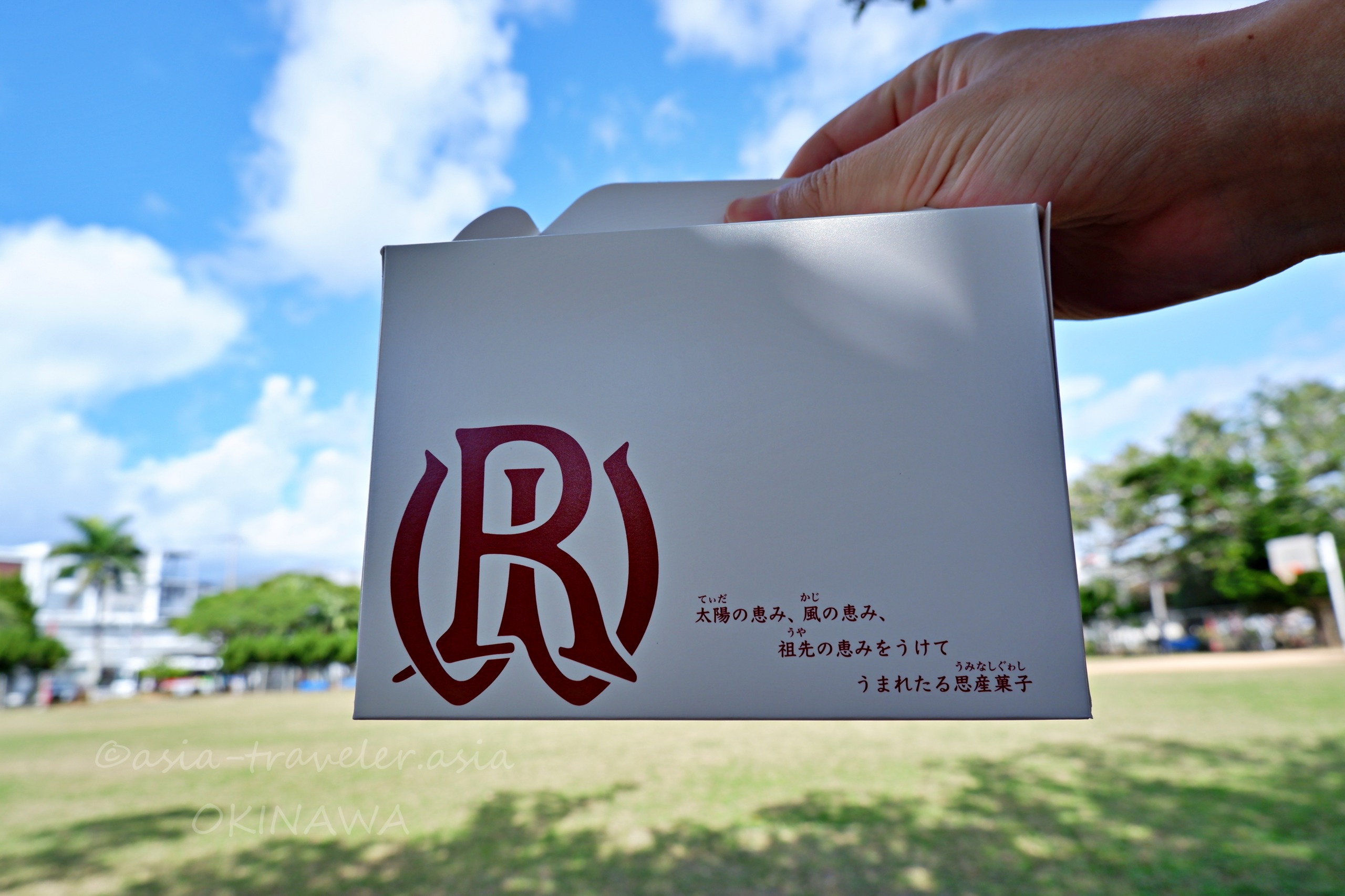 白バラ洋菓子店の白い菓子箱を与儀公園の青空の下で手に持つ様子