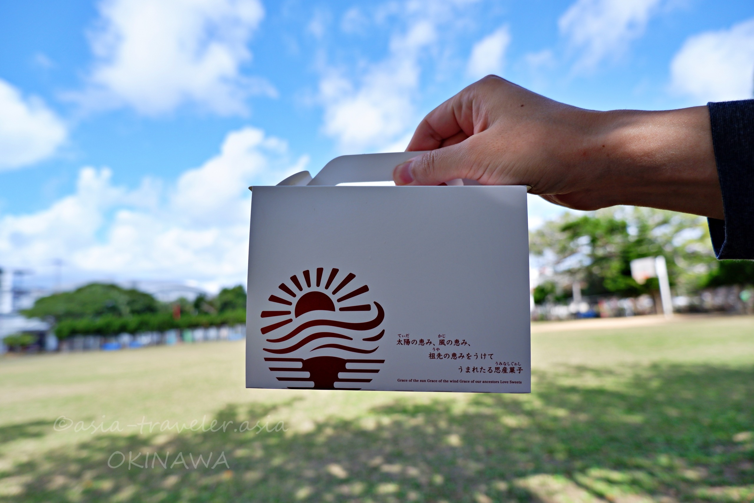 沖縄の青空の下で手に持つ白バラ洋菓子店の手提げ箱