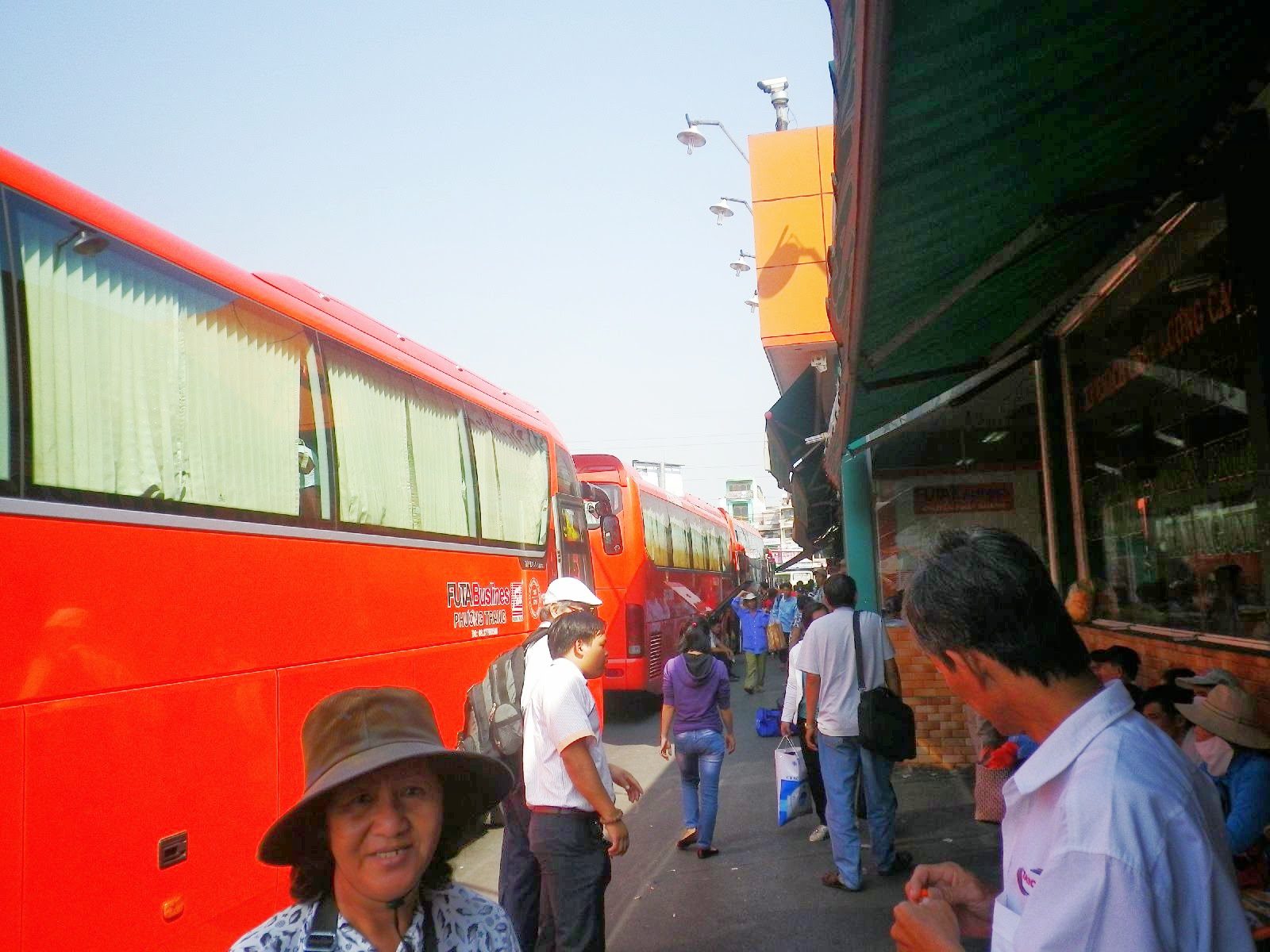 ホーチミンのバスターミナルに並ぶ赤い長距離バスと乗客たち
