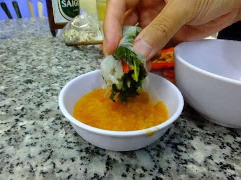 ゴイカーの生春巻きをオレンジ色のタレにつける手元