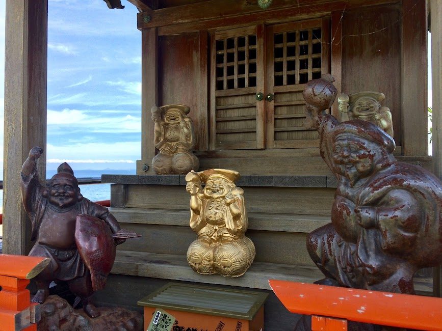 海辺の神社に並ぶ七福神の木彫り像と黄金の恵比寿像
