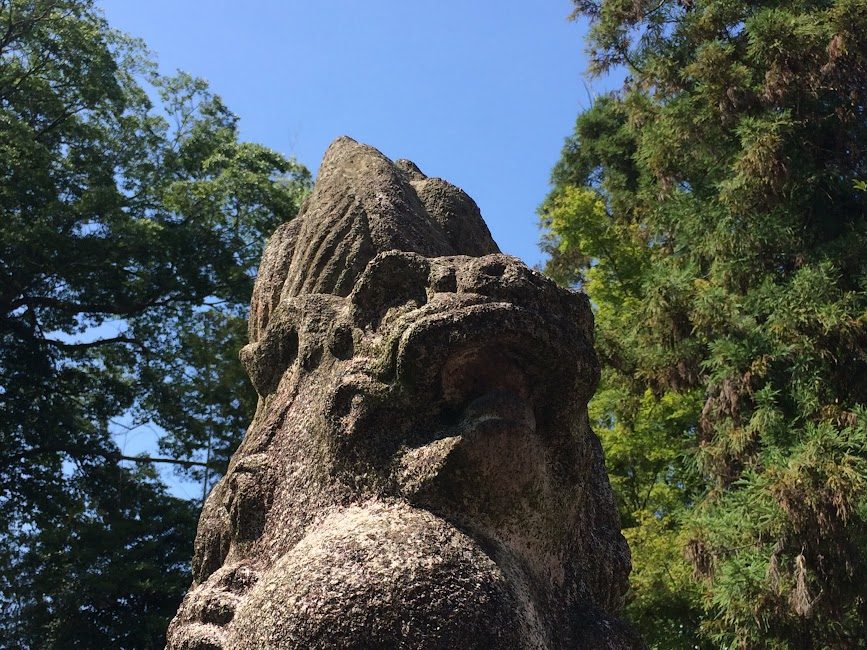 風化した石造りの狛犬を見上げるアングル