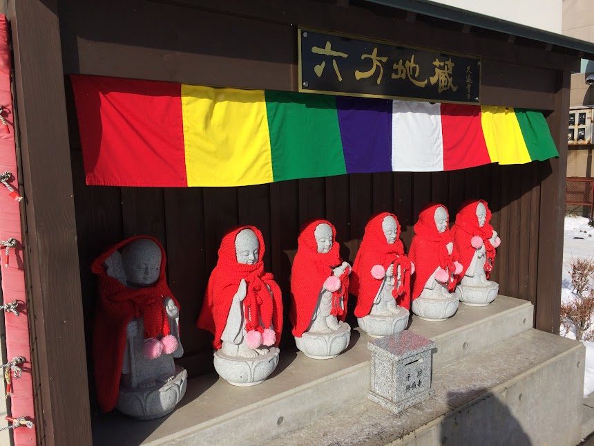 札幌の寺院に並ぶ赤い前掛けの六方地蔵と五色の幡