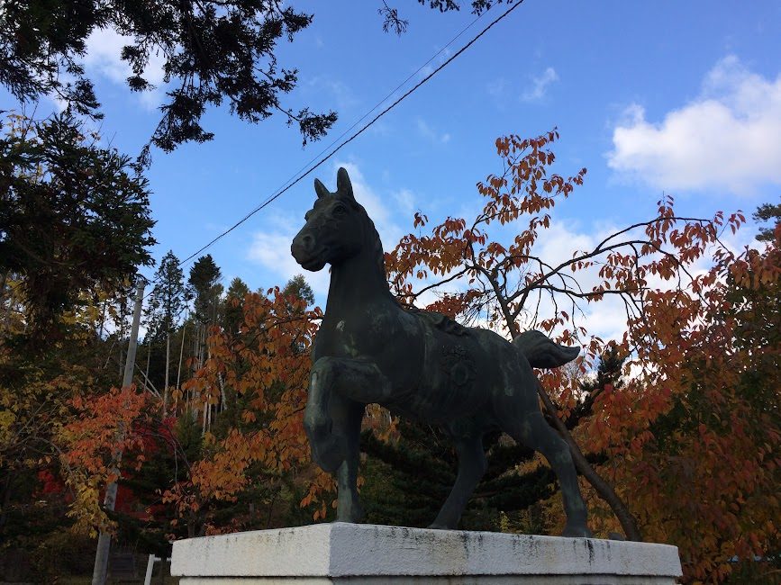 秋の紅葉を背景にそびえる馬の銅像