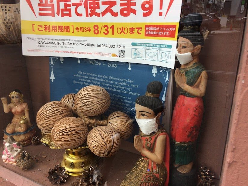 マスクを着けたタイ人形の置物と香川Go To Eatポスター