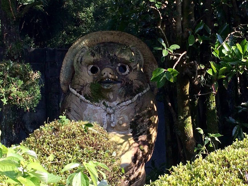 苔むした鬼面の石像が緑の庭木に囲まれる四国の神社
