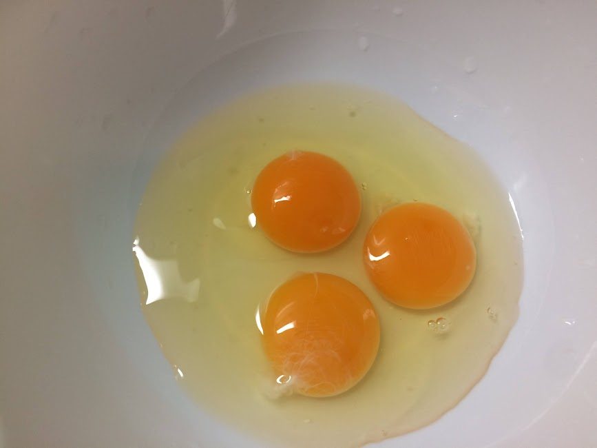 白いボウルに割り入れた鮮やかなオレンジ色の卵黄3つ