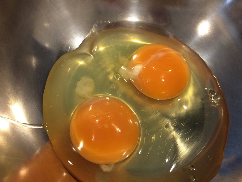 ステンレスボウルに割り入れた濃いオレンジ色の黄身の卵2個